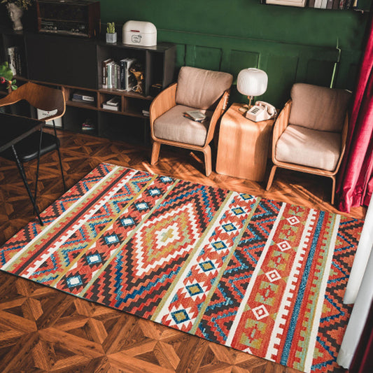 Colorful patterned rug on a wooden floor with chairs and a shelf in the background.